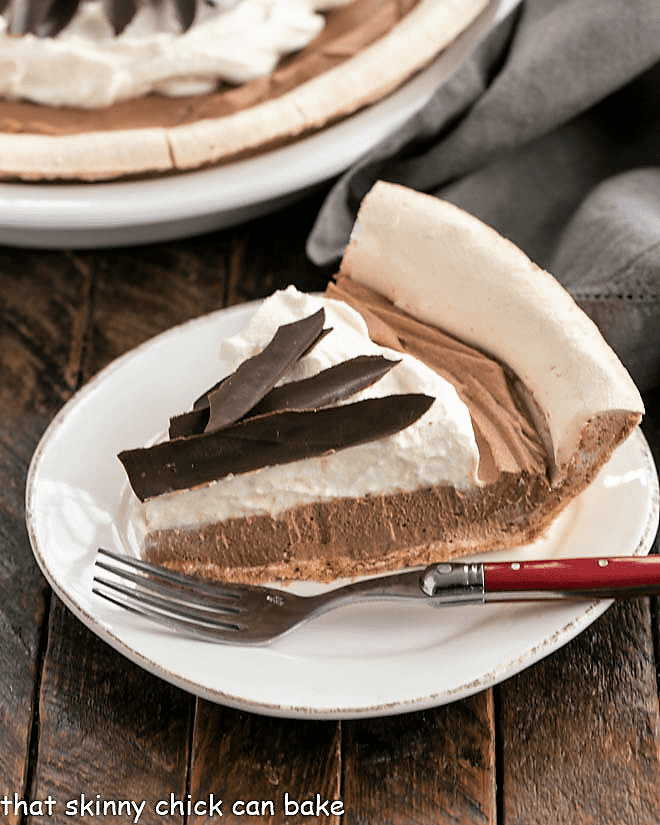 Slice of chocolate angel pie on a round white plate with a red handled fork