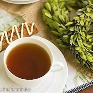 A gingerbread biscotti resting next to a cup of tea