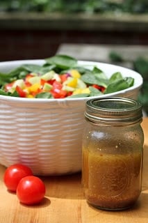 Gazpacho spinach salad in a white serving bowl with a mason jar of salad dressing.