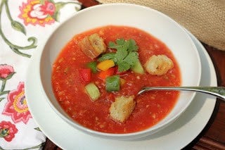 Gazppacho in a white bowl with toppings and a spoon