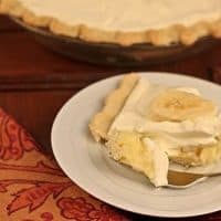 Slice of banana cream pie on a white plate with a fork holding a spoonful of the filling