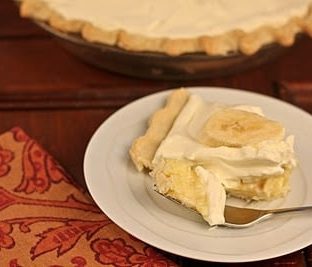 Slice of banana cream pie on a white plate with a fork holding a spoonful of the filling