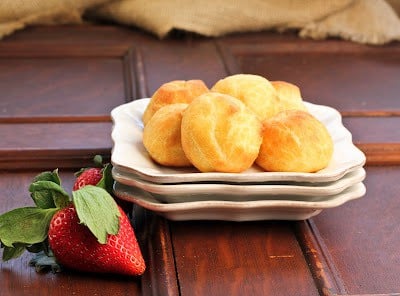 Cream puffs on a stack of white plates with fresh raspberries