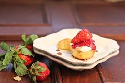 Cream puff filled with whipped cream and topped with berries on a stack of plates