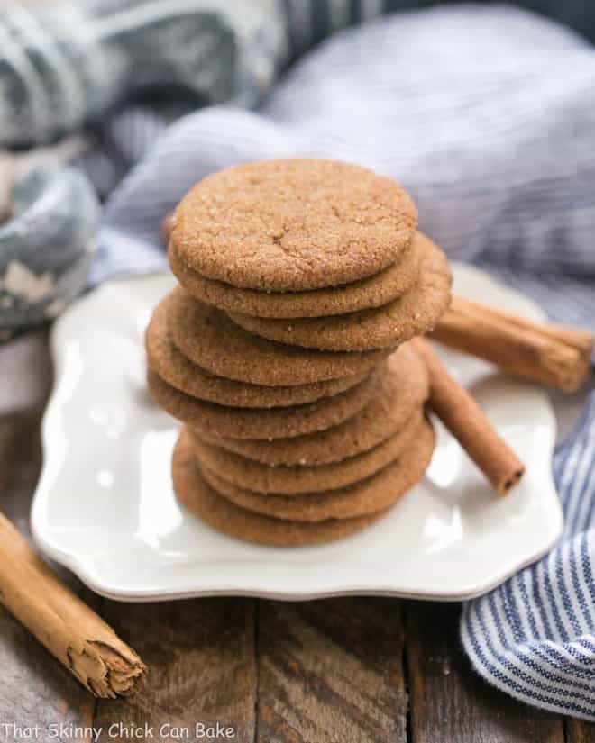 Holiday Ginger Crisps stacked on a white plate with cinnamon sticks