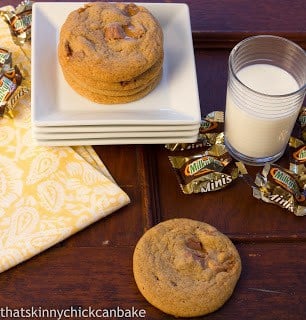 Milky Way Cookies on a stack of white serving plates next to Milky Way wrappers and a glass of milk. 