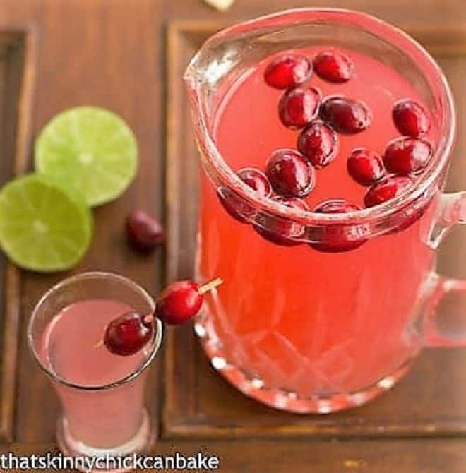 Pear cosmopolitans in a glass pitcher with fresh cranberry garnish