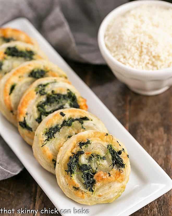 Muenster and Spinach Pinwheels on a narrow white tray with a bowl of grated Parmesan