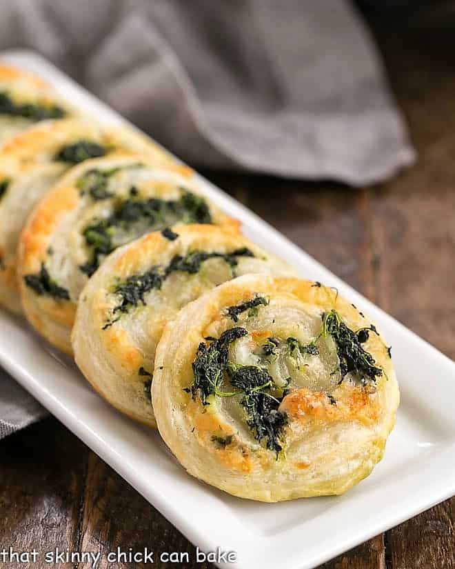 Muenster and Spinach Pinwheels lined up on a white, rectangle ceramic tray.