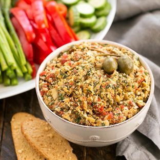 Roasted Red Pepper Artichoke Tapenade in a white bowl with a tray of crudite