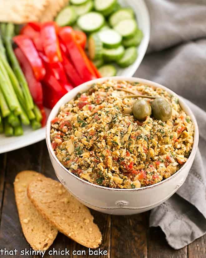 Roasted Red Pepper Artichoke Tapenade in a white bowl with a tray of crudite.