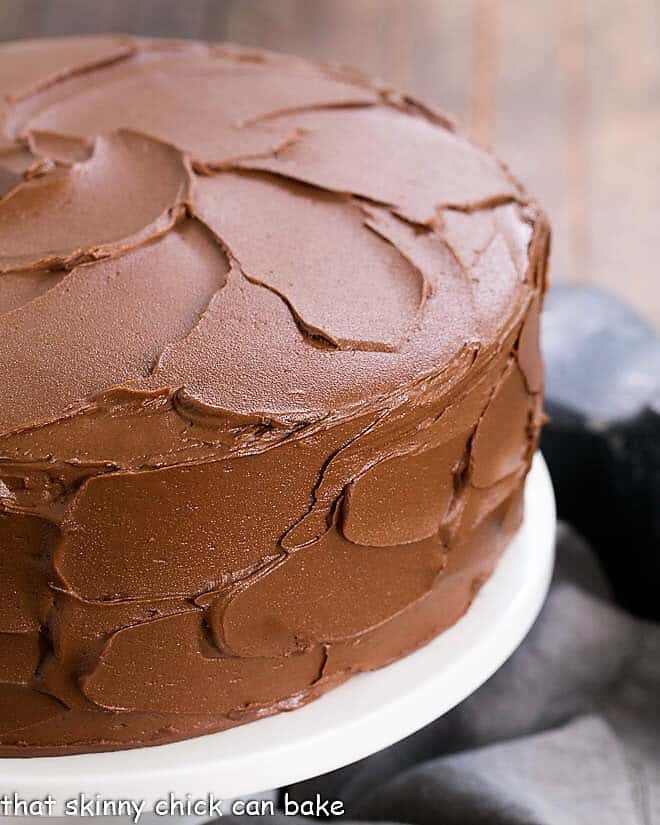 Chocolate Layer Cake with Ganache on a white ceramic cake stand.