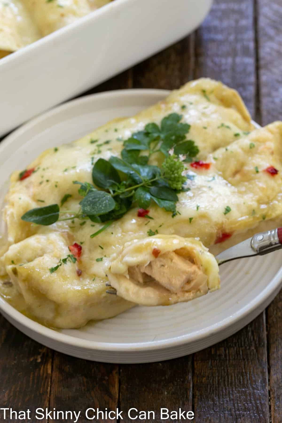 Creamy chicken enchilada on a white plate with a casserole dish in the background.