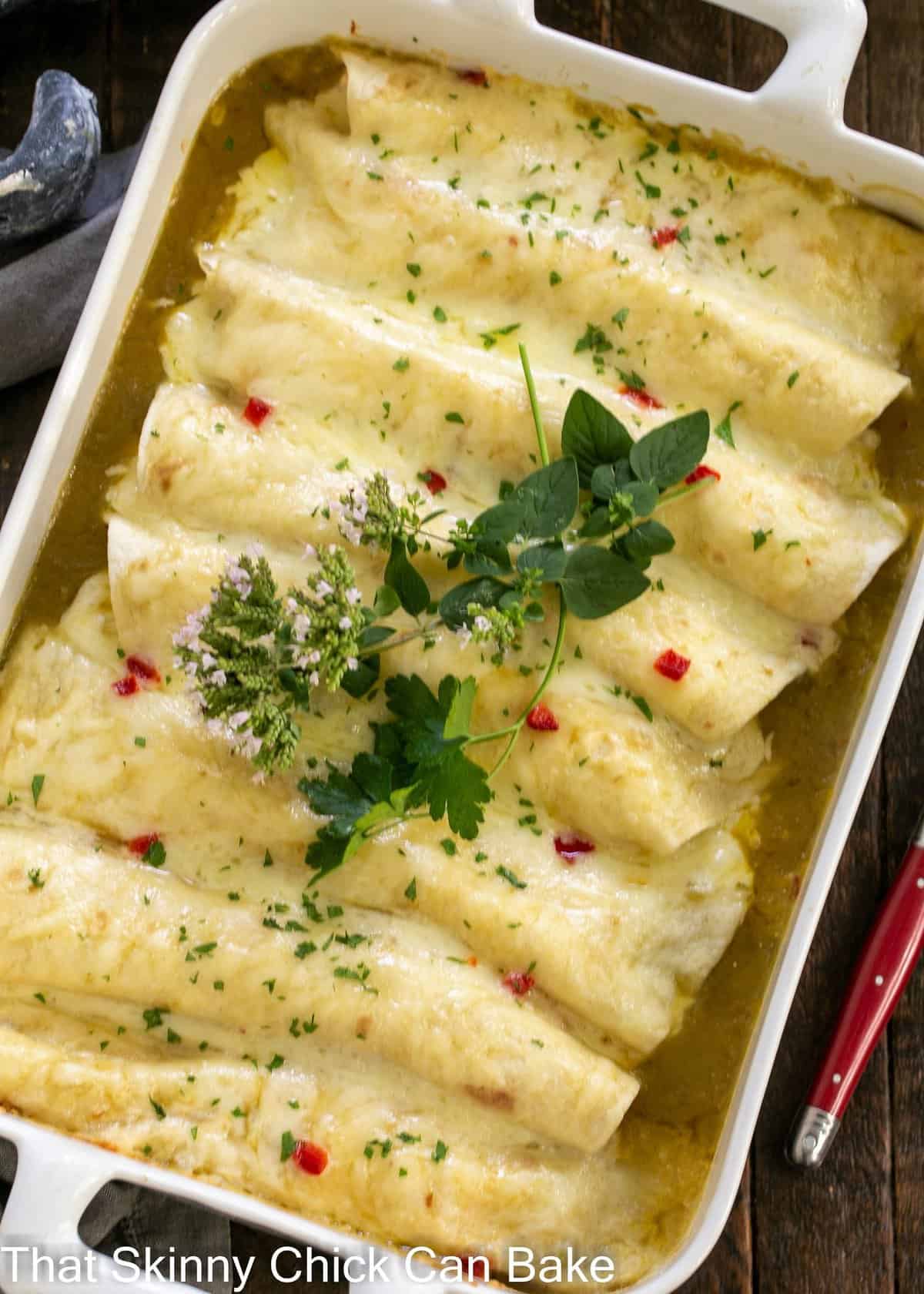 Overhead view of casserole full of green enchiladas topped with herb sprigs.