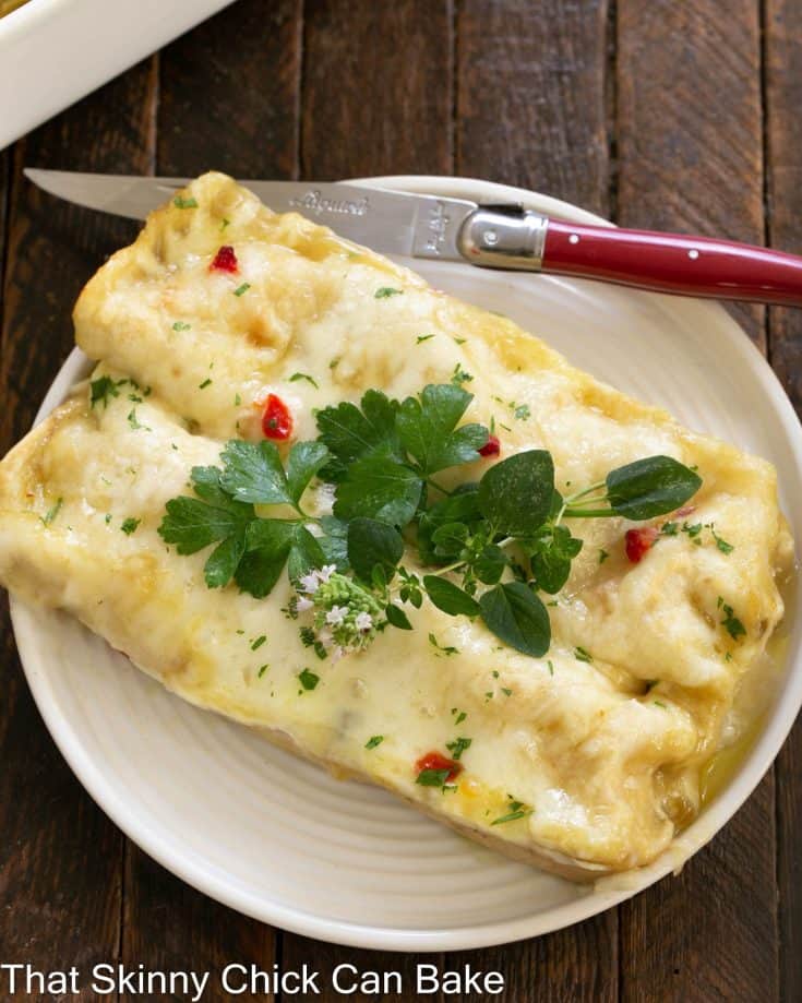 Overhead view of 2 green chicken enchiladas on a white plate with a red handled knife