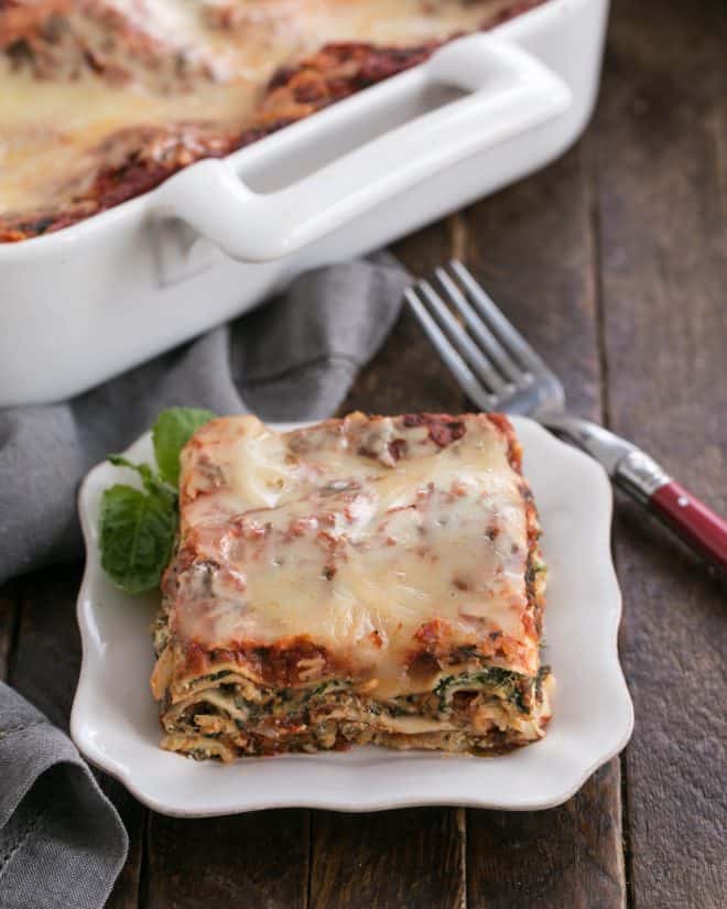 One slice of spinach lasagna on a white plate in front of the casserole dish