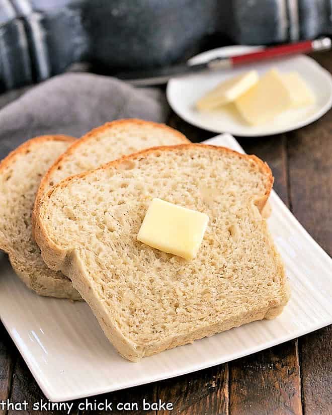 Three slices of oatmeal bread on a square plate with the top slice with a pat of butter