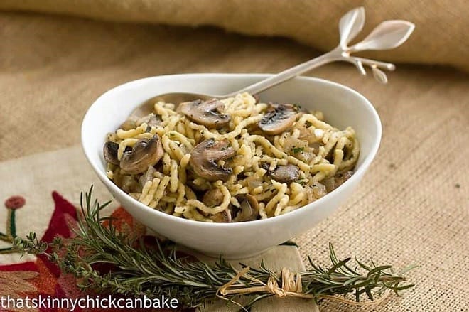 Herbed spaetzle with mushrooms in a white serving dish with a spoon