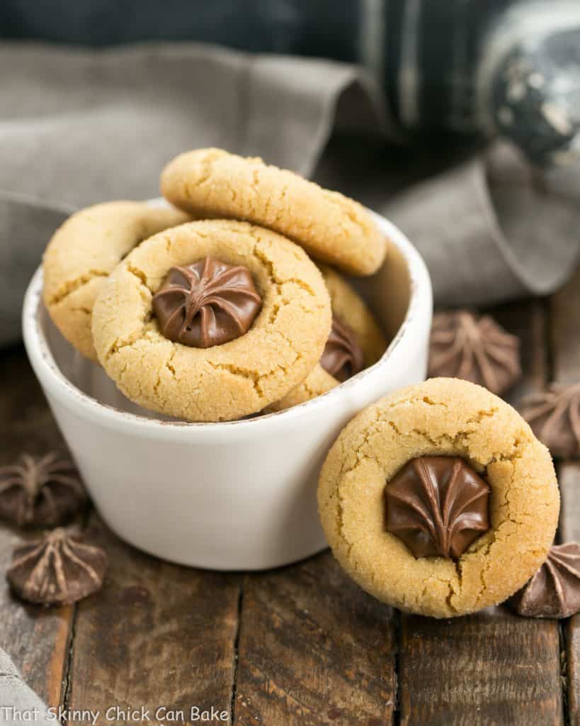 Peanut blossoms in a small white bowl with one cookie leaning on the bowl