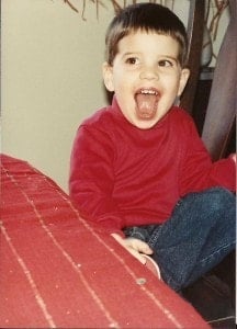 The birthday boy as a child in a red shirt and jeans with a big smile