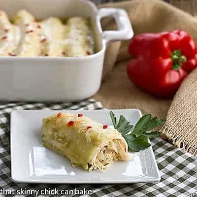 Creamy Chicken Enchiladas - an easy delicious weeknight meal! Creamy chicken enchilada on a white plate with a casserole dish in the background
