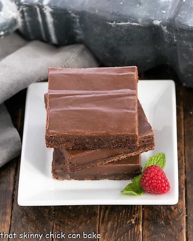 3 Fudge Topped Brownies stacked on a square white plate.