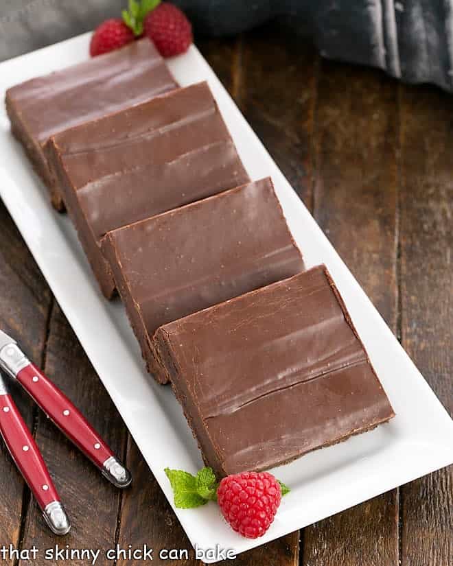 Fudge Topped Brownies on a white ceramic tray with a few fresh raspberries and mint garnishes.