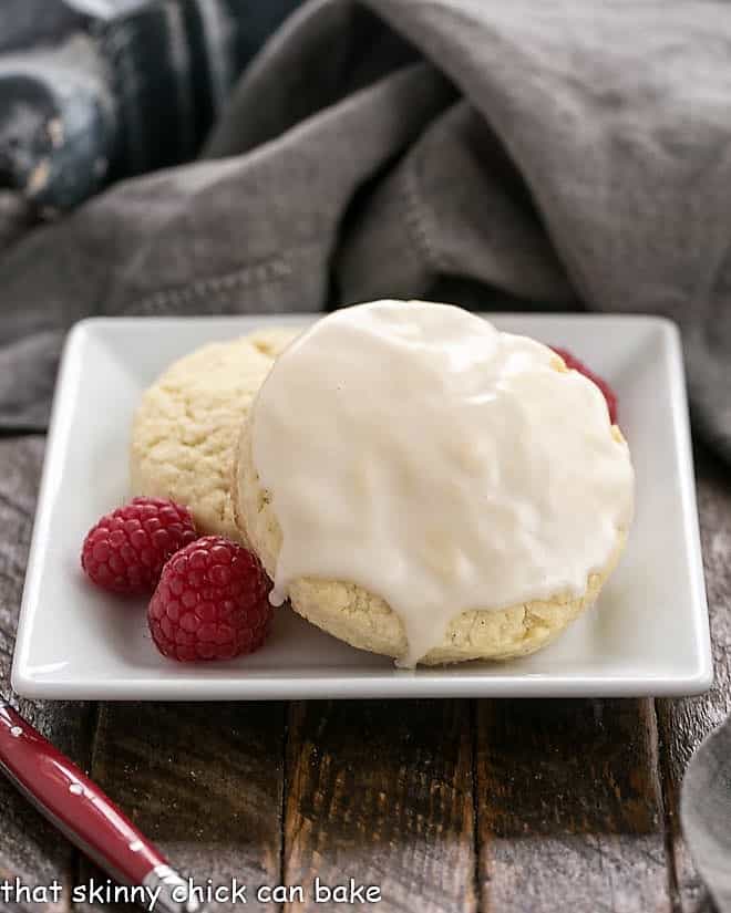 Two Super moist Vanilla Bean Scones on a square white plate with a few fresh raspberries.