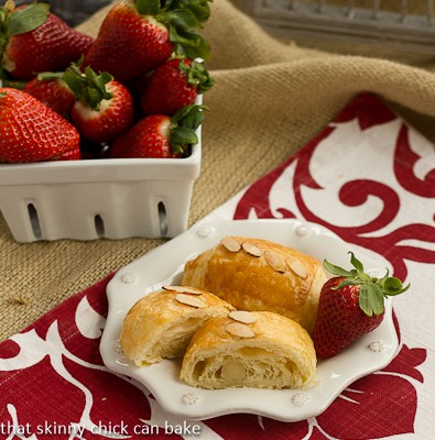 Almond croissants on a white plate on a red and white napkin with a bowl of fresh strawberries.