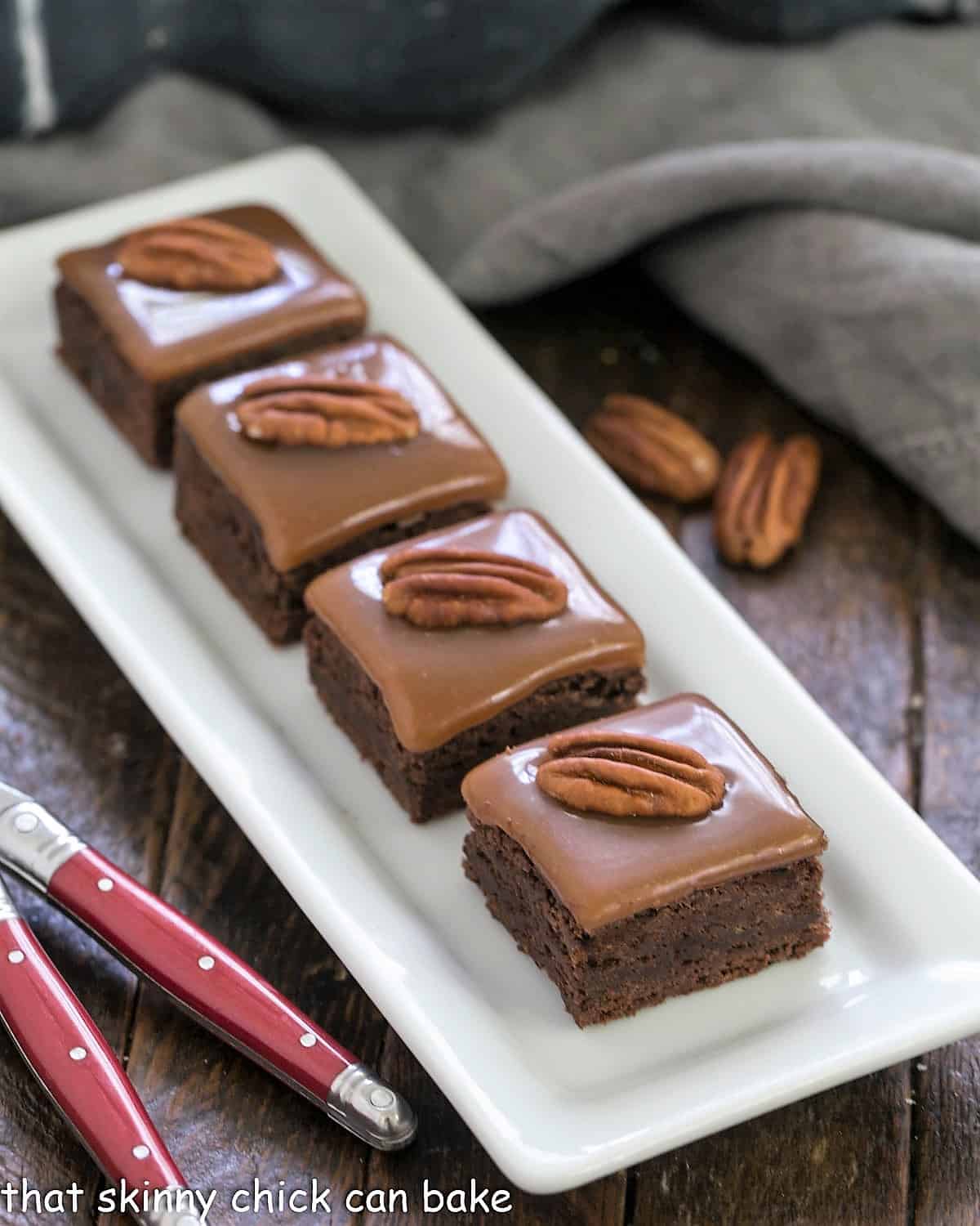 A white tray of caramel brownies with 2 red handled forks.