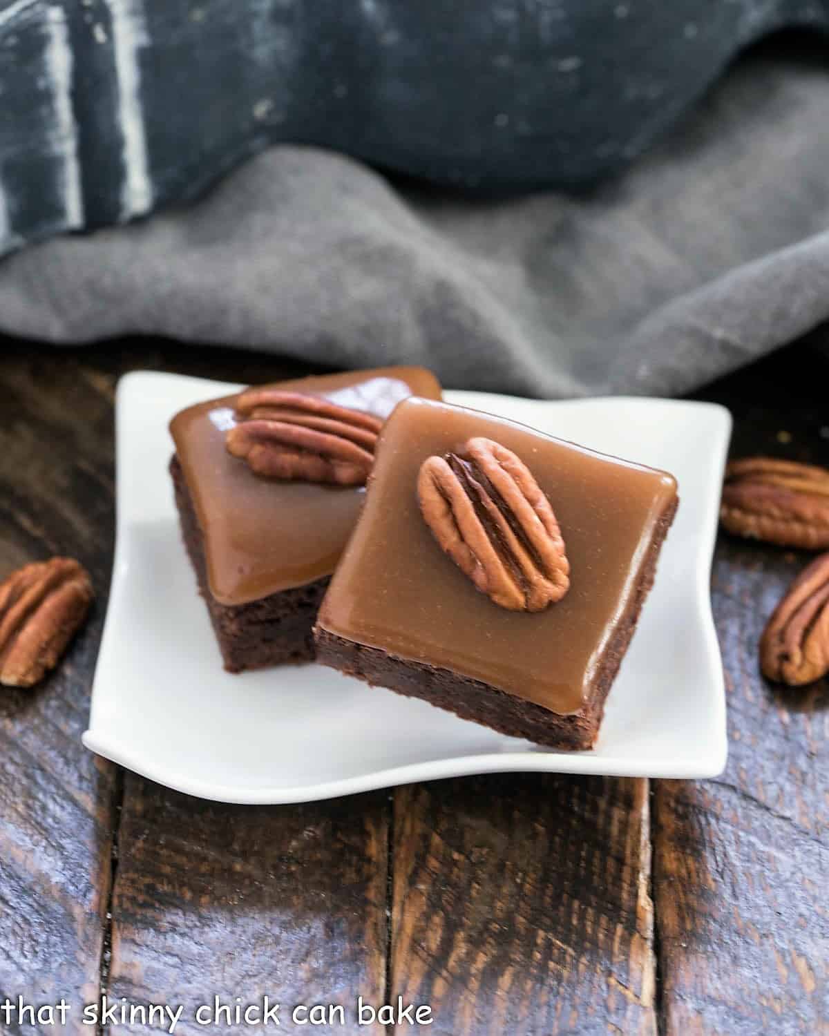 Two turtle brownies on a small white wavy plate.