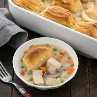 Small bowl of chicken pot pti with a biscuit atop in front of a casserole dish