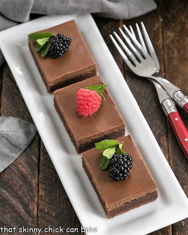 Ovehead view of 3 cheesecake brownies on a white tray topped with fresh berries.