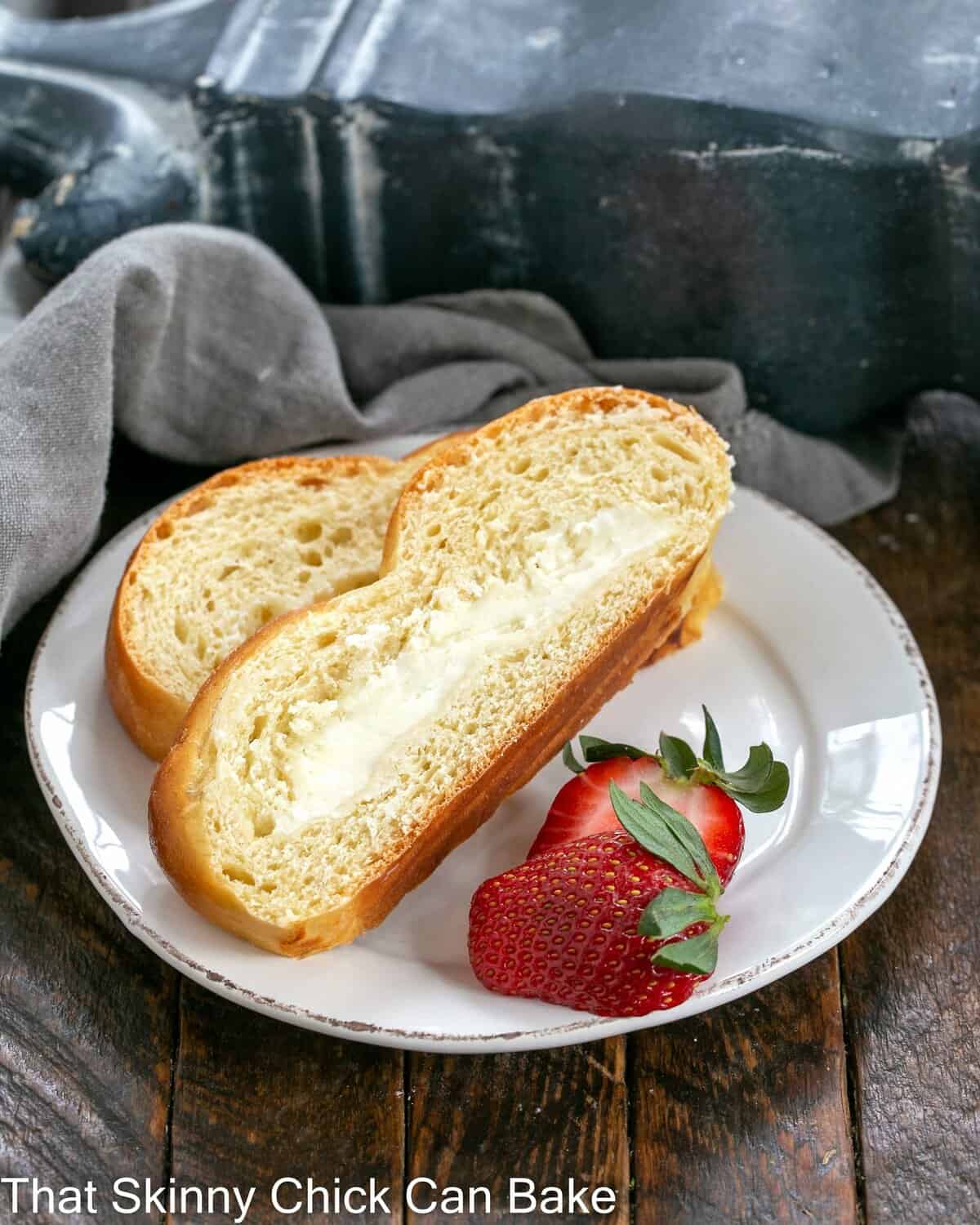 2 slices of braided easter bread on a white plate with strawberry garnish.