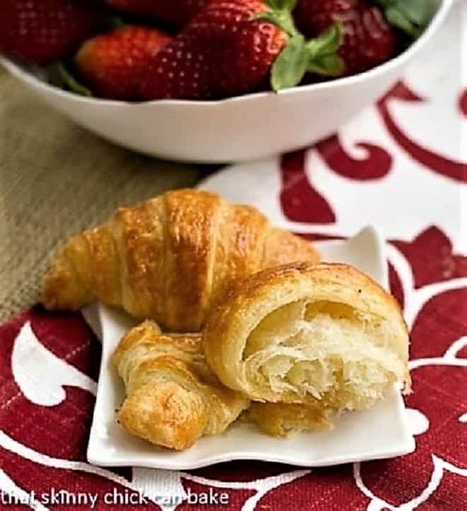 Homemade Classic Croissants on a small white ceramic plate with a bowl of strawberries