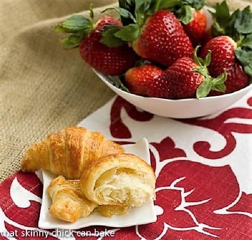 Homemade Classic Croissants with one broken open on a white plate with strawberries