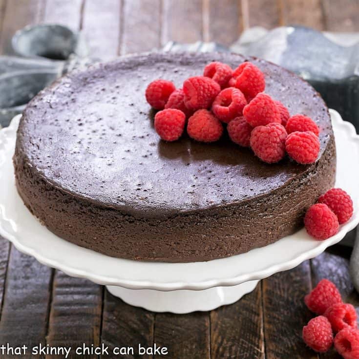 Flourless Kahlua cake on a white cake stand topped with raspberries