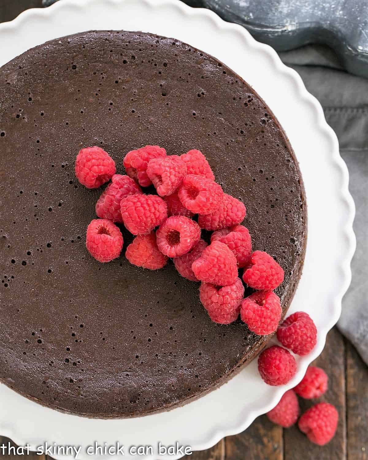 Overhead view of Flourless Chocolate Kahlua Cake topped with raspberries on a cake stand.