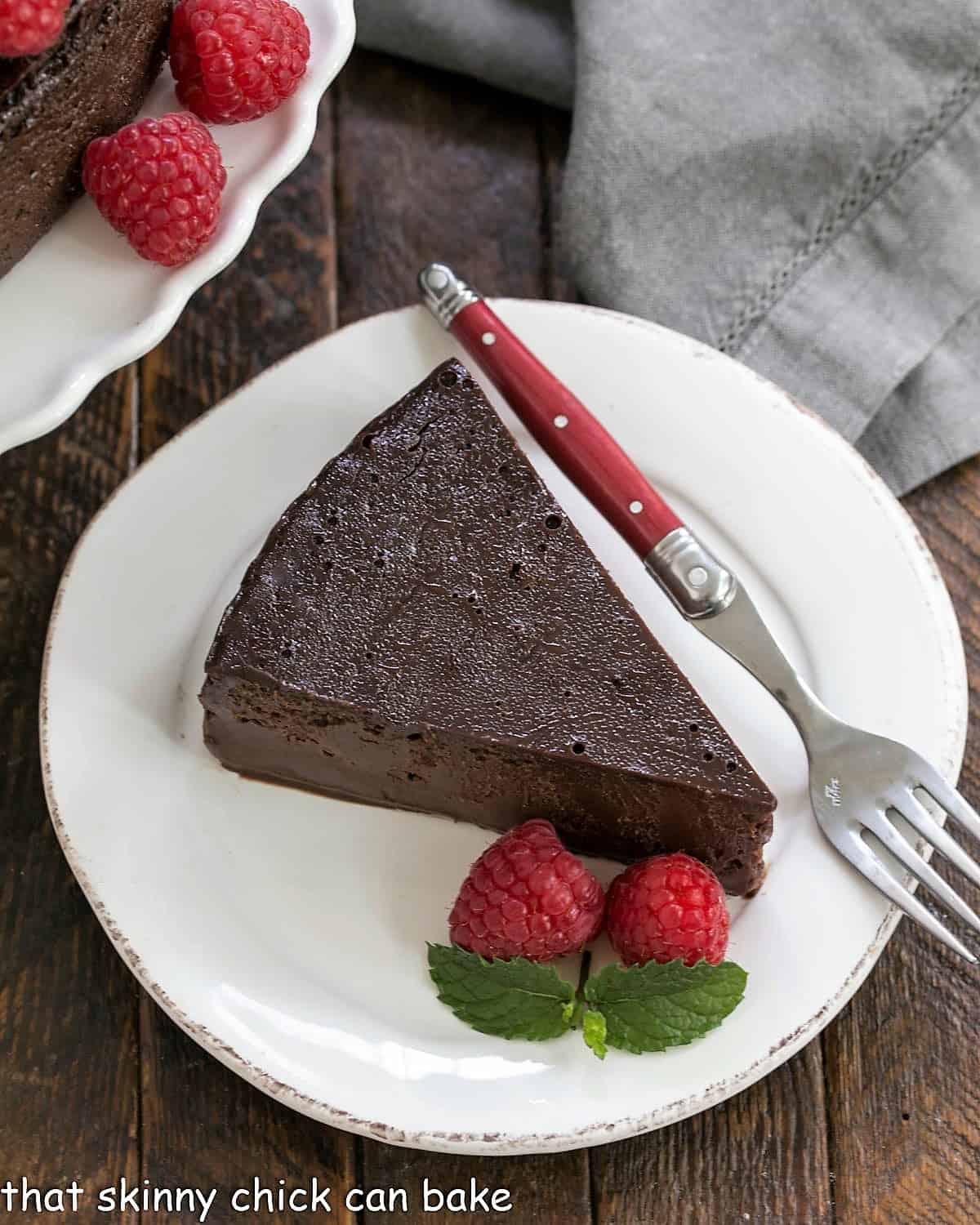 Flourless Chocolate Kahlua Cake slice on a white plate garnished with raspberries.