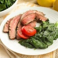 Lemon Steamed Spinach on a white dinner plate garnished with fresh tomatoes