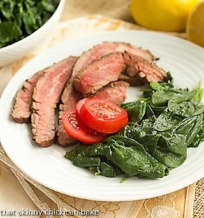 Lemon Steamed Spinach on a white dinner plate garnished with fresh tomatoes