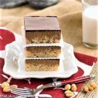 A stack of chocolate peanut butter krispie bars on a white plate over a red and white napkin