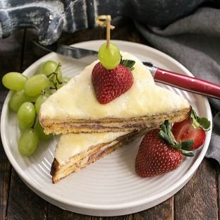 Croque-Monsieur Sandwich sliced and stacked on a white plate with grapes and strawberries