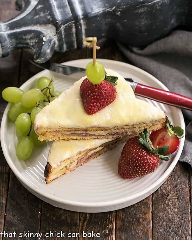 Croque-Monsieur Sandwich sliced and stacked on a white plate with grapes and strawberries.