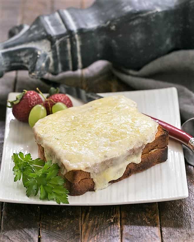 A Croque Monsieur on a white plate with a red handled knife