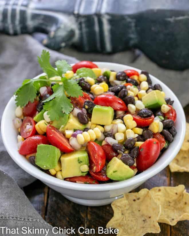 White serving bowl of corn salsa with a few scoops corn chips to the side