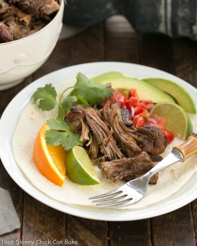 Slow cooked Pork Carnitas on a white plate with tomatoes, avocadoes and citrus