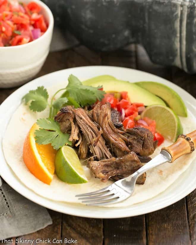 Slow cooked Pork Carnitas on a white plate with a bamboo fork.