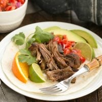 Slow cooked Pork Carnitas over a tortilla on a white plate