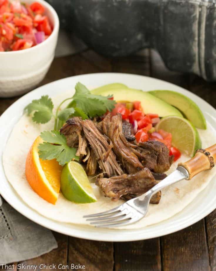 Slow cooked Pork Carnitas over a tortilla on a white plate